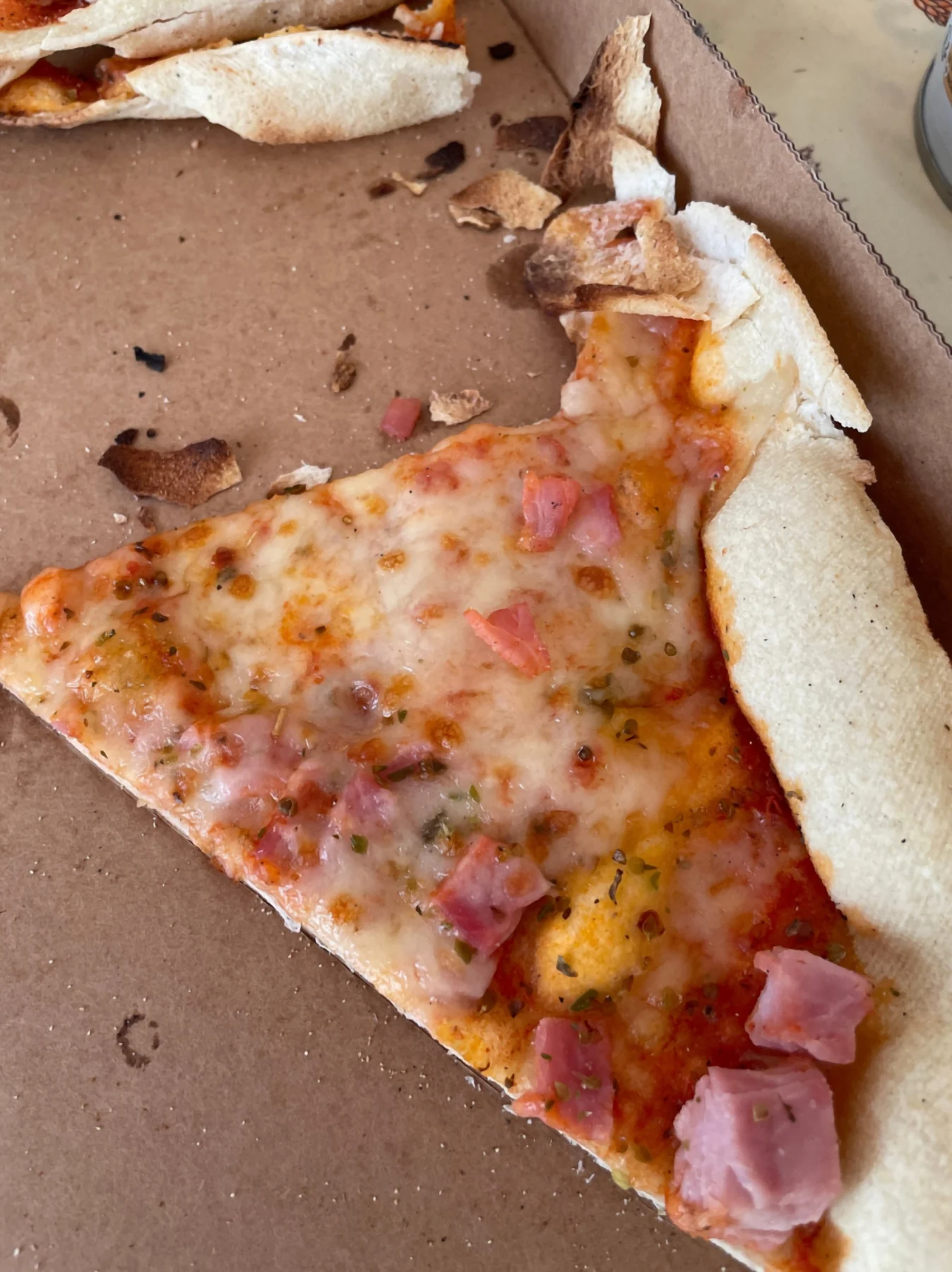Part de pizza au jambon, pâte fine croustillante sur carton kraft